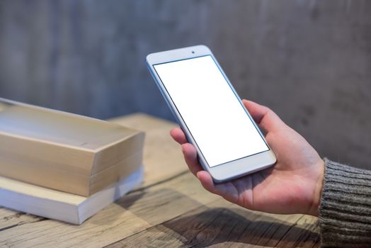 Woman holding a smartphone with books on a wooden table in a coffee shop