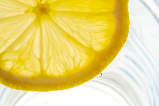 Lemon slice backlit in a glass of water close-up view