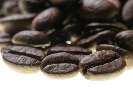 Heap of roasted coffee beans backlit on white close-up view