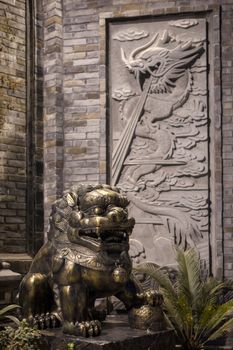 Lion bronze statue at with a dragon fresco on a brick wall at night in a chinese street in Chengdu, China