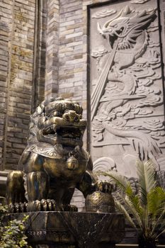 Lion bronze statue at with a dragon fresco on a brick wall at night in a chinese street in Chengdu, China