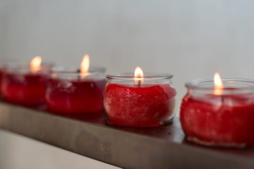 Four red candles in glass cups in row in a buddhist temple, Chengdu, China