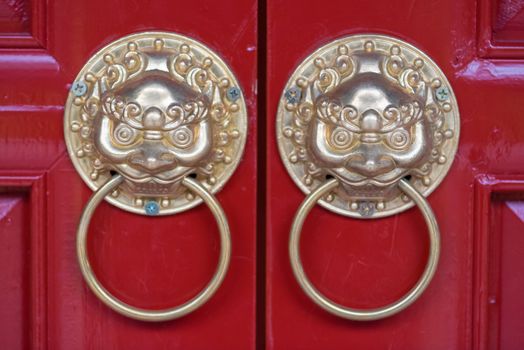 Golden colored chinese door knockers on a red door in China