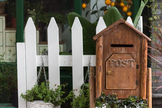 Wooden letter box with post inscription with plants and white fence in the background