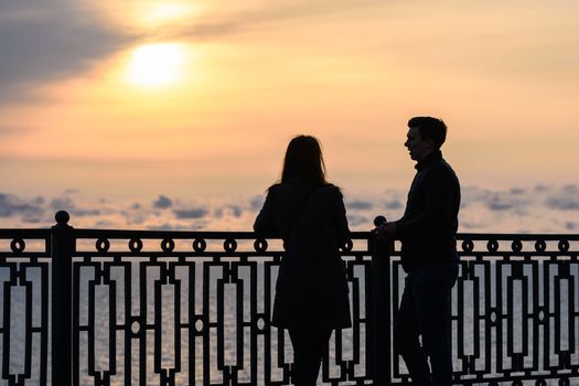 Two young people are talking while standing at sunset against the backdrop of the sea landscape