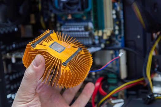 caucasian hand holding orange plated computer heatsink and pc internals in blurry background.
