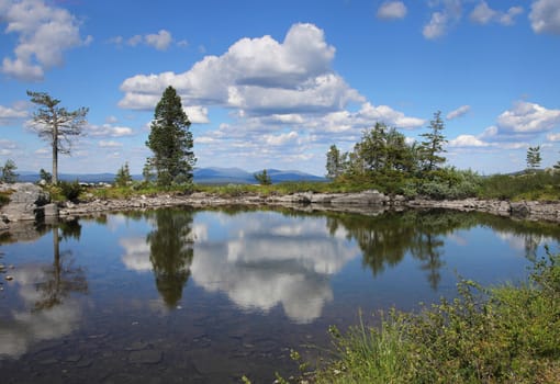 Small pond on Sarkitunturi fell top reflects the blue sky and white clouds
