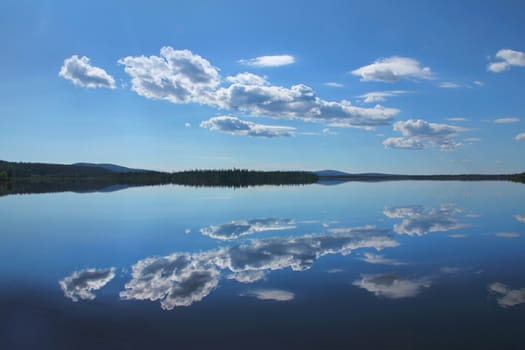 Calm blue Lake Akasjarvi reflects white clouds in Finnish Lapland