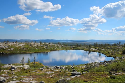 Small pond reflecting blue sky and white clouds on Särkitunturi fell top in Muonio, Lapland, Finland