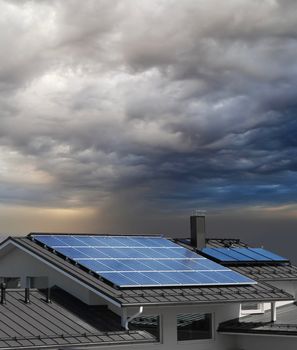 Solar panel system on house roof, stormy rain clouds approaching
