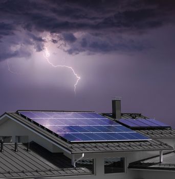 Solar panel system on house roof, dark sky, thunder and lightning background