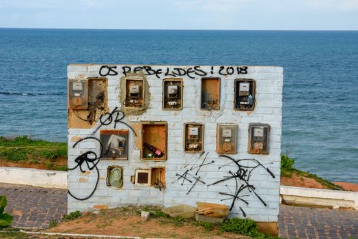 Old and broken electric meter boxes on a wall in front of the sea on Brazil
