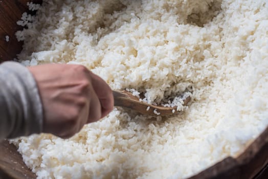 Hand taking white rice with a wooden spoon in a large  container