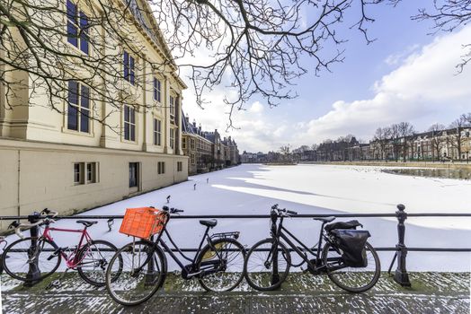 Rusty bicycles in front of the panoramic view of the Dutch parliament building and its frozen pond water