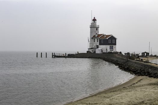 View of the white Marken island lighthouse under a foggy and cold skyline in the early morning, Netherlands