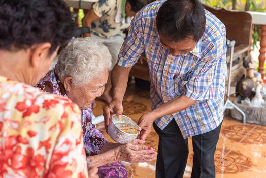 Ang Thong, Thailand - April 7, 2019 : Unidentified Asian people bathe respectation to elderly parents by water with jasmine, rose flower and aromatherapy in bowl in Songkran Festival (Thai New Year)