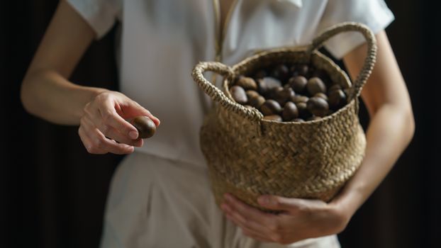 Person holding chestnuts on hand with wicker basket full of chestnuts.