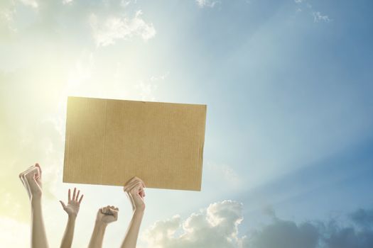 Woman's hands holding a blank banner to put the text at protesting with clear sky and sunlight background.
