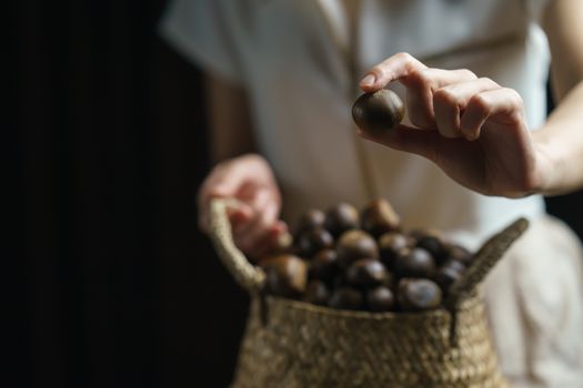 Person holding chestnuts on hand with wicker basket full of chestnuts.