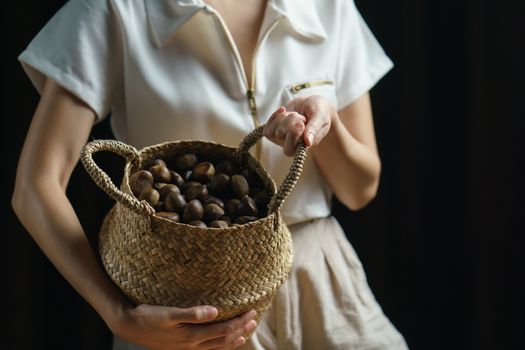 Person holding chestnuts on hand with wicker basket full of chestnuts.
