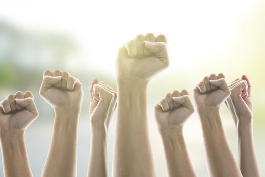 People in city raised fists in the air, sunlight background. victory and protest