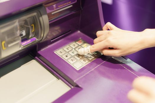 Woman wearing rubber for finger pressing a button of Automated Teller Machine( ATM )