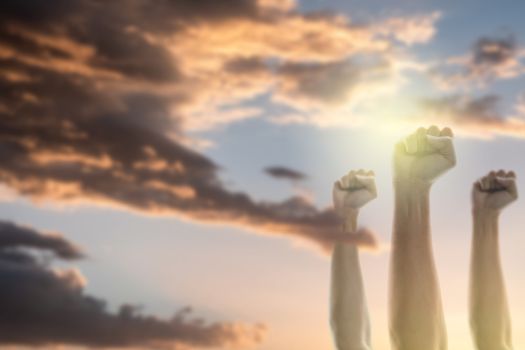 Fists of people raised in the air with sky and sunlight background.