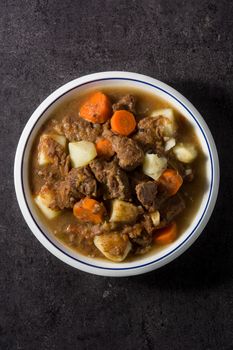 Irish beef stew with carrots and potatoes on black background