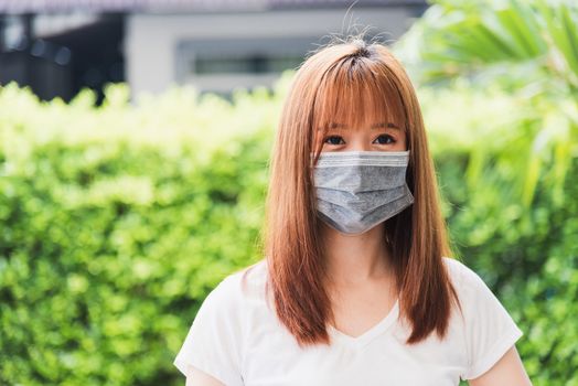 Asian young woman wearing face mask protective outdoor under quarantine pandemic coronavirus COVID-19 on green nature background