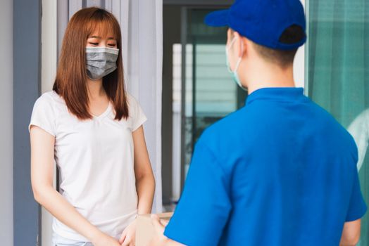 Asian young delivery man courier with package post box in uniform he protective face mask he making service woman customer receiving front house under curfew quarantine pandemic coronavirus COVID-19