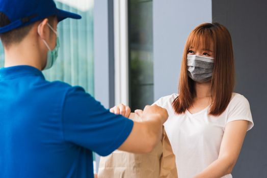 Asian delivery express courier young man giving paper bags fast food to woman customer receiving both protective face mask, under curfew quarantine pandemic coronavirus COVID-19