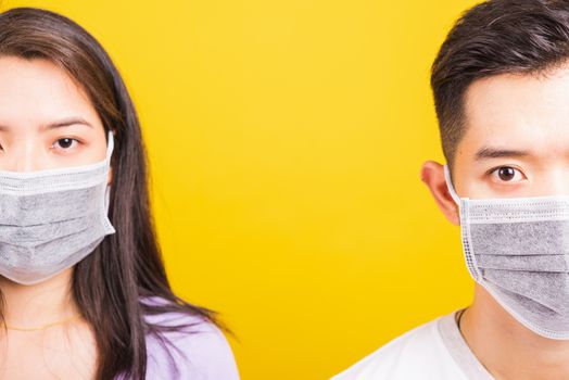 Asian beautiful woman and handsome man wearing protection face mask against coronavirus, looking to camera, studio shot isolated on yellow background with copy space, COVID-19 or corona virus concept