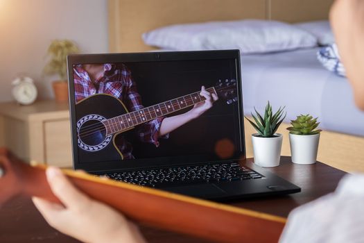music academy online lesson concept. teenage spend their free time doing interesting activity at home by learning to play guitar chord from website via laptop computer application.