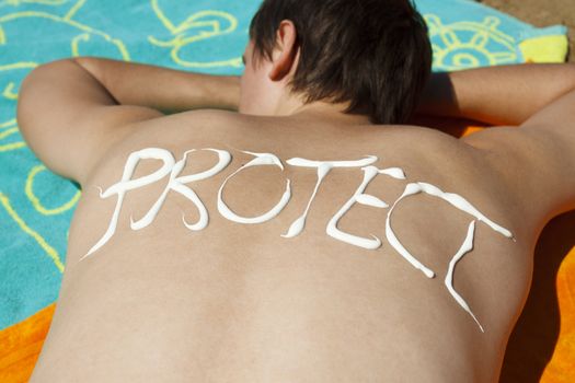 Man lying down at beach and protect written on his back with sunscreen.