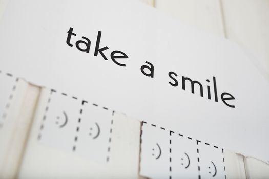 A paper with the phrase: Take a Smile and with a smile sign ready to be tore off. DOF. The focus is on the a letter.