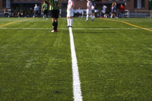 Detail of lines of soccer field with soccer players at background and out of focus.