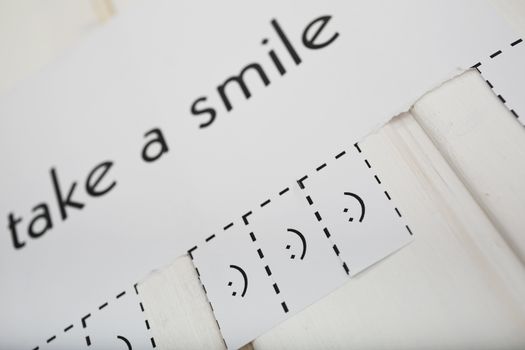 A paper with the phrase: Take a Smile and with a smile sign ready to be tore off. DOF. The focus is on the smile sign.