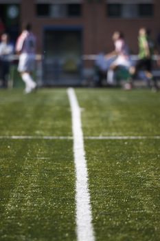 Detail of lines of soccer field with soccer players at background and out of focus.