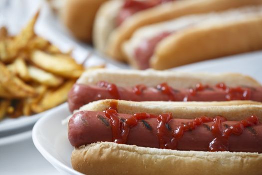 Hot dogs with fries and ketchup and more hot dogs at background.