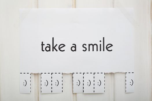 A paper with the phrase: Take a Smile and with a smile sign ready to be tore off. The photo is front. 