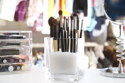 Beauty organizer of brushes for make up and make up itself, with cloths hanging at background.