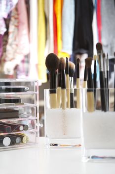 Beauty organizer of brushes for make up and make up itself, with cloths hanging at background.