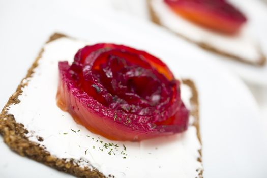 Appetizer of marinated salmon over a black bread with dill dyed with beetroot.