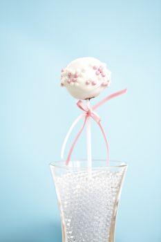 A single cakepop over blue background with pink ribbon.