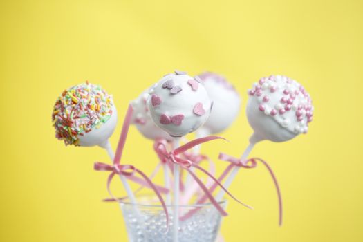 Cakepops over yellow background with pink ribbon.