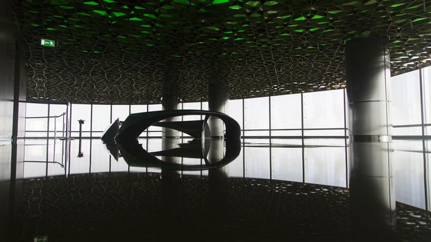 Spacious floor from a skycraper. The camera is situated on the floor. There is nothing in the room but a monument in the middle. It is a contrast between the outside light, the indoors dark. The frame covers from floor to ceiling.