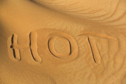 The word hot writen on the sand in desert.