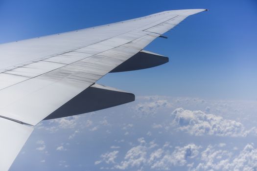 View from the right side of an aircraft of the wing, the plane is ready to land. It is a sunny day with a clear blue sky with clouds beneath it.