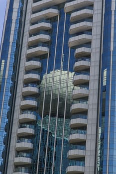 There is a building reflected on the surface of another building. The main building is mirrored and actual modern design. The blue color gives a business look.