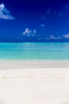 Word love written on sand in Maldives with the lagoon at background.